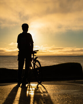 Silhouette image of a cyclist watching the sunrise at Milford beach, Auckland. Vertical format.