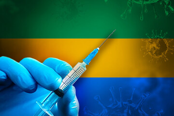 Gabon Covid-19 Vaccination Campaign. Hand in a blue rubber glove holds a syringe with covid-19 virus vaccine in front of Gabon flag