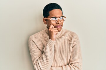 Young handsome hispanic man wearing turtleneck neck sweater and glasses thinking concentrated about doubt with finger on chin and looking up wondering