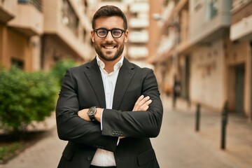 Young hispanic businessman with arms crossed smiling happy at the city.