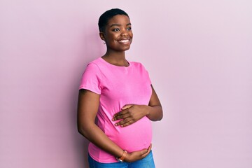 Young african american woman expecting a baby, touching pregnant belly looking away to side with...