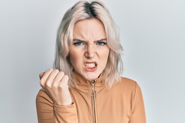 Young blonde girl wearing casual clothes angry and mad raising fist frustrated and furious while shouting with anger. rage and aggressive concept.