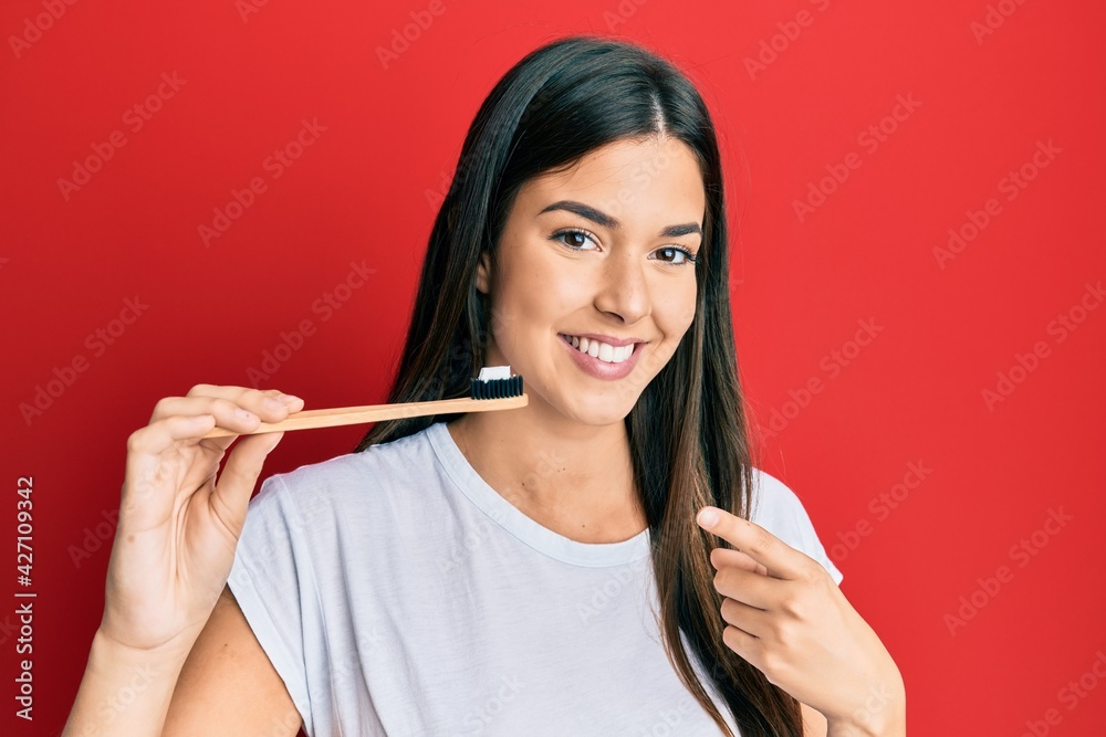 Poster young brunette woman holding toothbrush with toothpaste smiling happy pointing with hand and finger