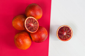 Half and whole ripe juicy sicilian blood oranges on pink and white background, top view. Red orange