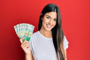 Young brunette woman holding hong kong 50 dollars banknotes looking positive and happy standing and smiling with a confident smile showing teeth