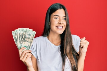 Young brunette woman holding 20 dollars banknote screaming proud, celebrating victory and success very excited with raised arm