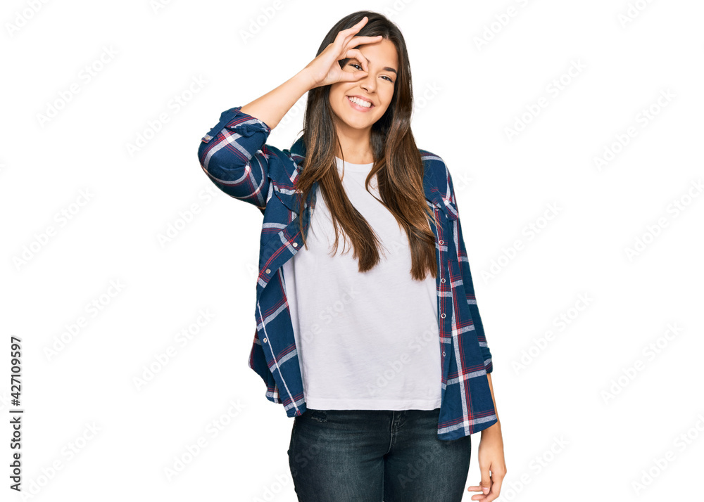 Wall mural Young brunette woman wearing casual clothes smiling happy doing ok sign with hand on eye looking through fingers