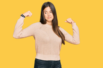 Young brunette woman wearing casual winter sweater showing arms muscles smiling proud. fitness concept.