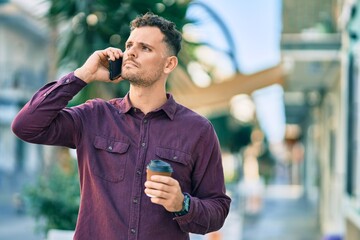 Young hispanic man with serioys expression talking on the smartphone and drinking coffee at the...