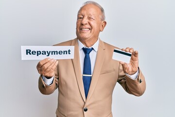 Senior caucasian man holding payment word paper and credit card winking looking at the camera with sexy expression, cheerful and happy face.