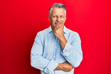 Middle age grey-haired man wearing casual clothes looking confident at the camera with smile with crossed arms and hand raised on chin. thinking positive.