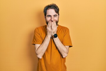 Caucasian man with beard wearing casual yellow t shirt laughing and embarrassed giggle covering...