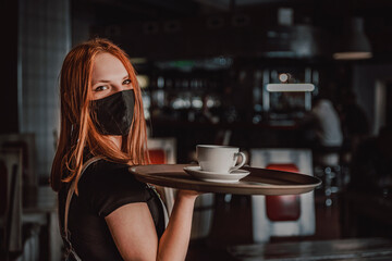 Portrait young waitress standing in cafe. girl the waiter holds in bunches a tray with utensils. Restaurant service