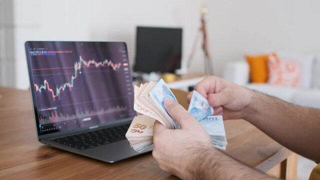 The man who watches cryptocurrency and digital money graphics from his home on a leptop. man examining stock market charts while counting his cash. The new generation of money making method is digital