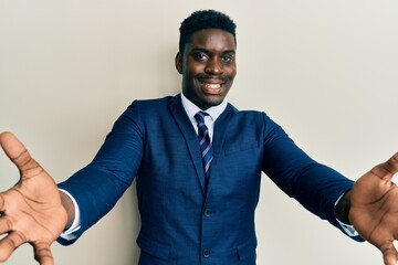 Handsome black man wearing business suit and tie looking at the camera smiling with open arms for hug. cheerful expression embracing happiness.