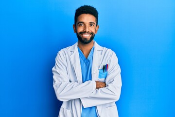 Handsome hispanic man with beard wearing doctor uniform happy face smiling with crossed arms looking at the camera. positive person.