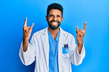 Handsome hispanic man with beard wearing doctor uniform shouting with crazy expression doing rock symbol with hands up. music star. heavy concept.