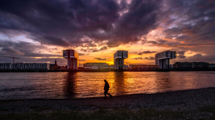 Fototapeta na wymiar The image was shot in the beautiful city of Köln with the gorgeous Kranhäuser im Rheinauhafen and a magnificent golden hour sky and a sillouhette of an unknown passer by in the foreground.
