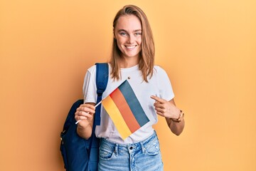 Beautiful blonde woman exchange student holding germany flag smiling happy pointing with hand and finger
