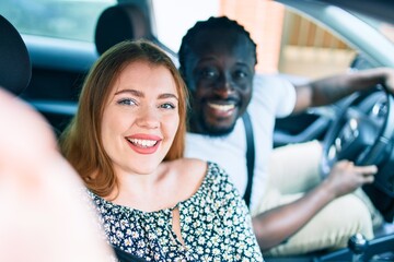 Young interracial couple smiling happy making selfie by the camera at the car.