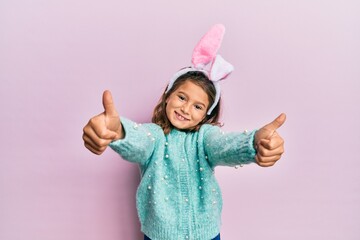 Little beautiful girl wearing cute easter bunny ears approving doing positive gesture with hand,...