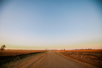 Fototapeta na wymiar Dirt country road at dusk with moon visible in the clear sky