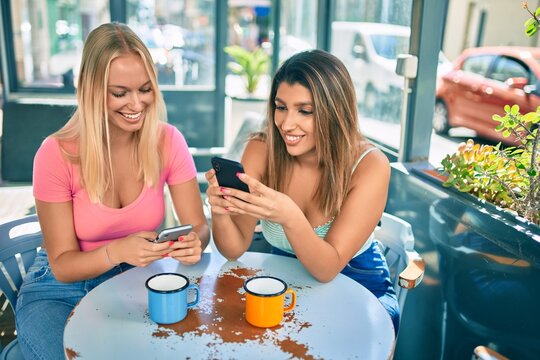 Two beautiful and young girl friends together at cafeteria using smartphone