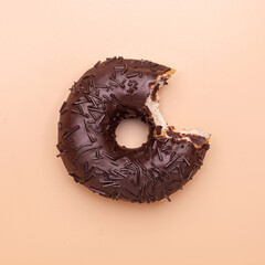 bitten donut with chocolate glaze and sprinkles isolated on brown background