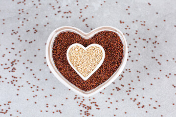 Red and white Quinoa in heart-shaped bowl on stone background.