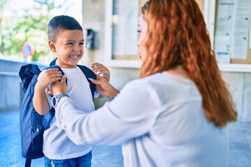 Adorable latin student boy and mom at school. Mother preparing kid putting up backpack.