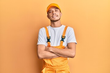 Hispanic young man wearing handyman uniform happy face smiling with crossed arms looking at the camera. positive person.