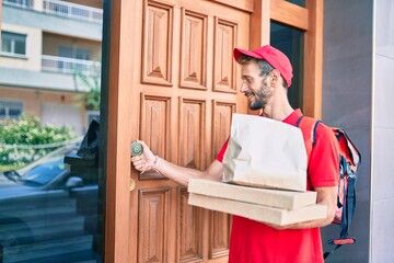 Caucasian delivery man wearing red uniform and delivery backpack smilly happy outdoors holding pizza box