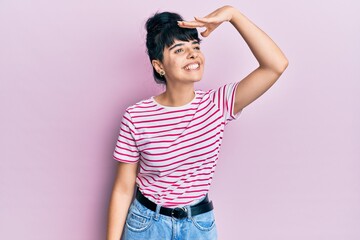 Young hispanic girl wearing casual clothes very happy and smiling looking far away with hand over head. searching concept.