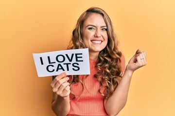 Young blonde girl holding paper with i love cats phrase screaming proud, celebrating victory and success very excited with raised arm