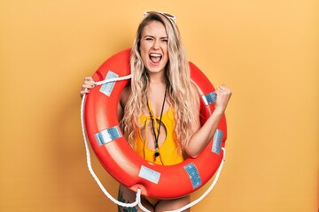 Beautiful young blonde woman wearing bikini and holding lifeguard float screaming proud, celebrating victory and success very excited with raised arms