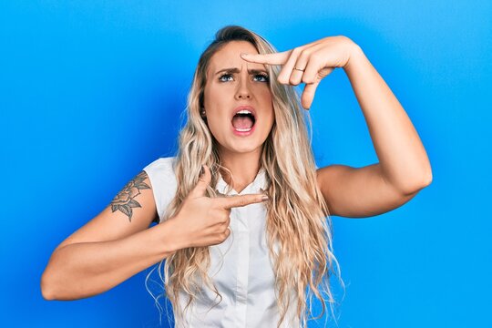 Beautiful young blonde woman doing picture frame gesture with hands angry and mad screaming frustrated and furious, shouting with anger looking up.