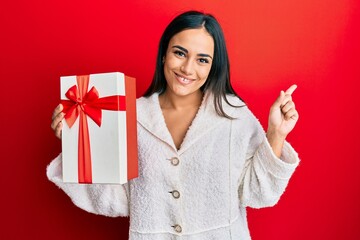 Young brunette woman holding gift smiling happy pointing with hand and finger to the side