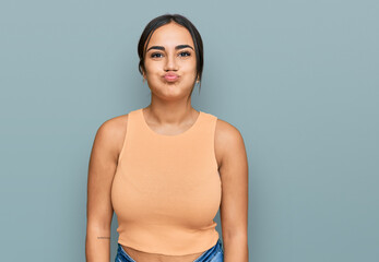 Young brunette woman wearing casual clothes puffing cheeks with funny face. mouth inflated with...