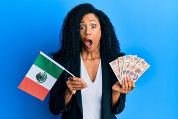 Middle age african american woman holding mexico flag and mexican pesos banknotes afraid and shocked with surprise and amazed expression, fear and excited face.