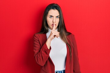 Young brunette teenager wearing business jacket asking to be quiet with finger on lips. silence and secret concept.