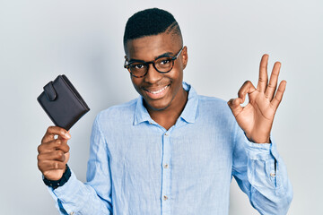 Young african american man wearing glasses holding leather wallet doing ok sign with fingers, smiling friendly gesturing excellent symbol