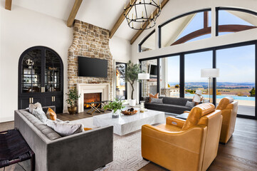 Beautiful living room in new luxury home. Features vaulted ceilings, stone fireplace surround, chandelier, fireplace with roaring fire, and gorgeous exterior view with infinity pool and valley.