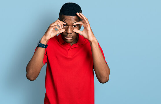 Young african american man wearing casual red t shirt trying to open eyes with fingers, sleepy and tired for morning fatigue