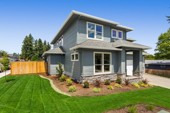 Exterior of new home on bright sunny day with blue sky. Features two car garage, front yard with green grass, and modern design