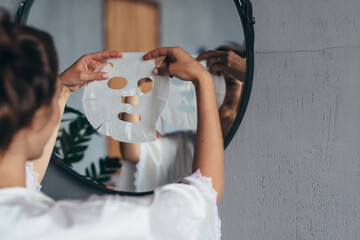 Woman with sheet mask in her hands in the bathroom before applying it to her face