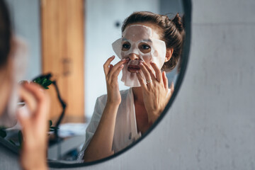 Home skin care. A woman applies a sheet mask to her face