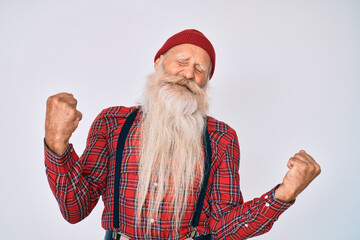 Old senior man with grey hair and long beard wearing hipster look with wool cap very happy and excited doing winner gesture with arms raised, smiling and screaming for success. celebration concept.