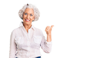 Senior grey-haired woman wearing casual clothes smiling with happy face looking and pointing to the side with thumb up.