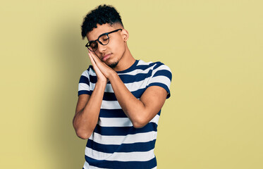 Young african american man wearing casual clothes and glasses sleeping tired dreaming and posing...