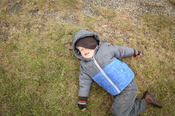 Top down view of little boy lying on grass in winter wearing thick jacket with hoodie